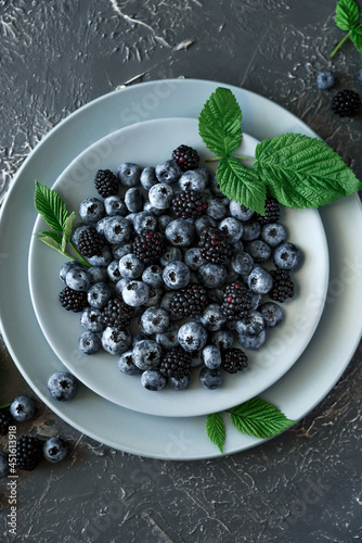 Fresh blueberries and blackberries decorated green leaves on gray concrete background. Top view