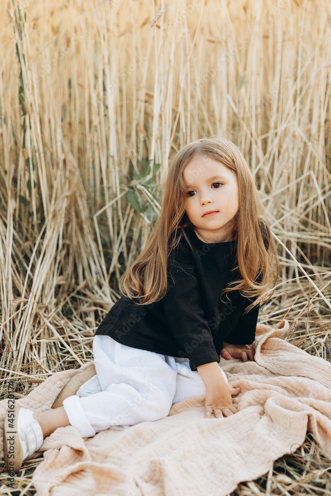 pretty 3-year-old girl walks and poses for a photo in a wheat field at sunset