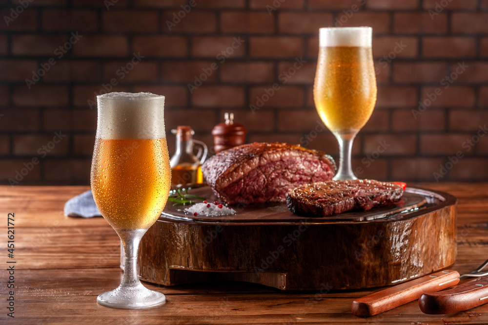 Two sweaty cold tulipa glasses of beer with grilled sliced cap rump steak  on wooden cutting board (Brazilian picanha). Stock Photo | Adobe Stock