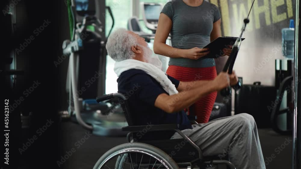 Disability old man works with personal trainer at health club. Senior man exercising with the assistance from female personal trainer Disability old man works with personal trainer at health club. Senior man exercising with the assistance from female personal trainer