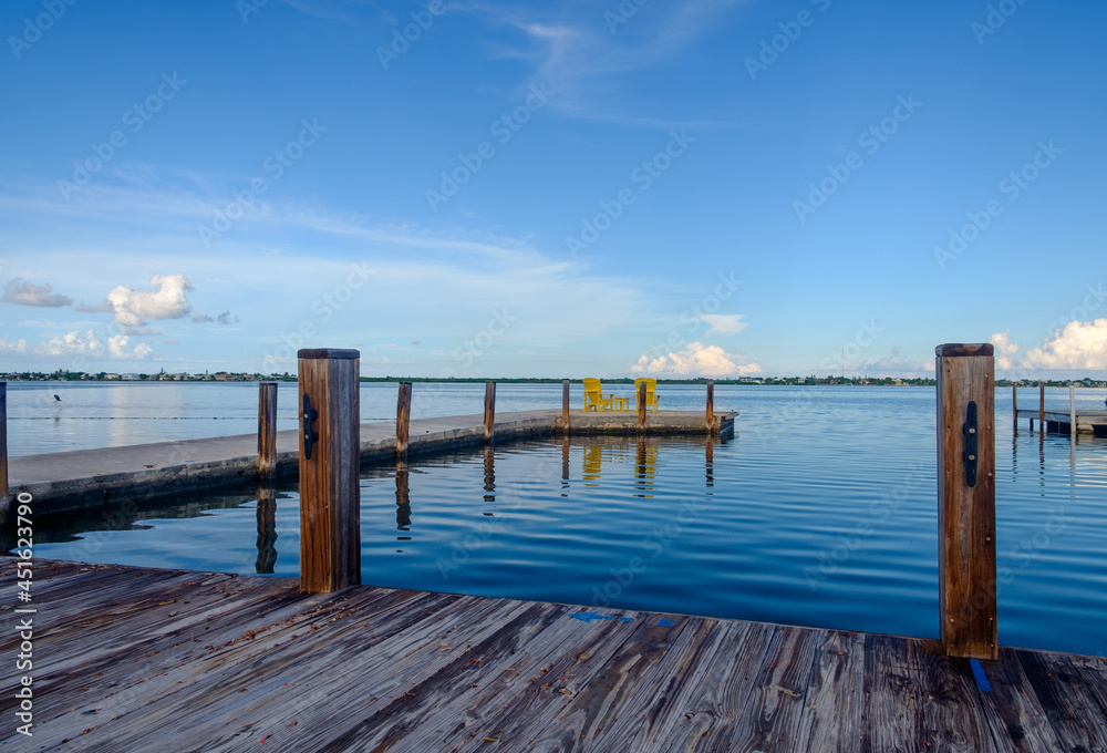 A set of yellow adirondack chairs sit at the end of a wooden and concrete in the florida keys at the end of the beautiful sunny day on vacation