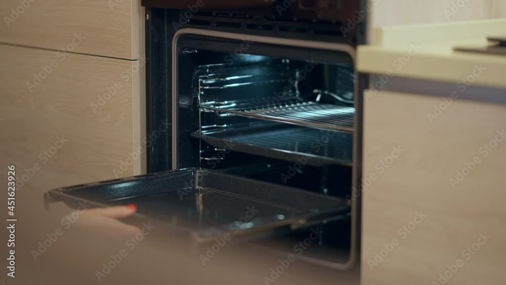 Female Caucasian hand pulling out baking sheets from shiny brand new oven in shop. Unrecognizable woman choosing household appliance in store indoors in slow motion Female Caucasian hand pulling out baking sheets from shiny brand new oven in shop. Unrecognizable woman choosing household appliance in store indoors in slow motion