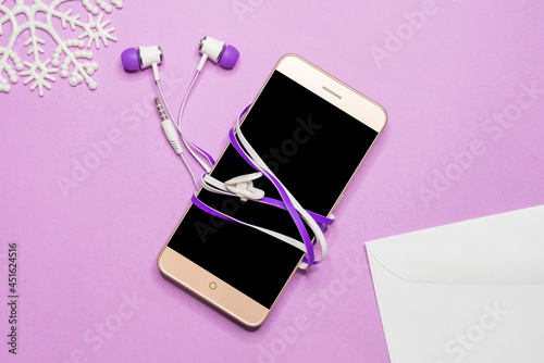 A smartphone with headphones is lying on a lilac table.