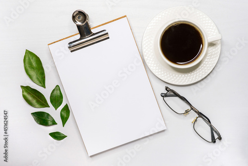 Tablet on the table with a white sheet of paper, glasses and a mug with coffee