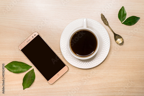A smartphone, a mug of coffee and a spoon lie on the table obliquely.