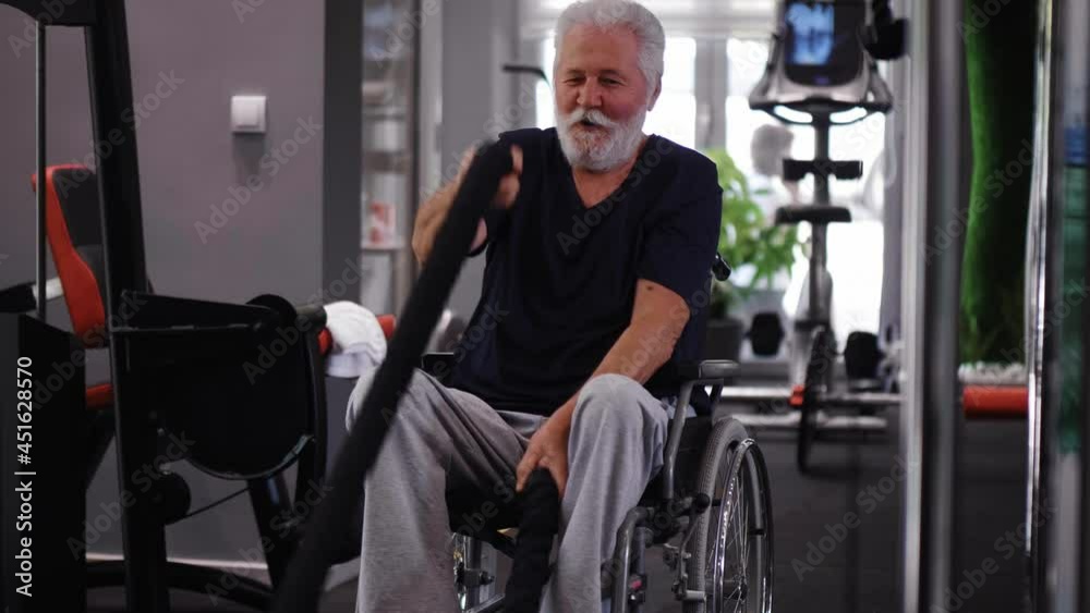 Disabled old man doing exercises with two ropes in a gym. Slow motion Disabled old man doing exercises with two ropes in a gym. Slow motion