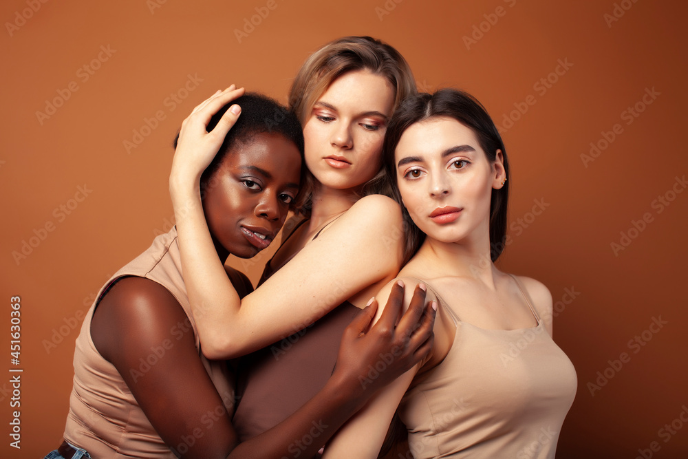 young pretty caucasian, afro, scandinavian woman posing cheerful together on brown background, lifestyle diverse nationality people concept young pretty caucasian, afro, scandinavian woman posing cheerful together on brown background, lifestyle diverse nationality people concept