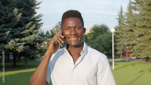 beautiful African American man walks down the street, talking on the phone, in the summer