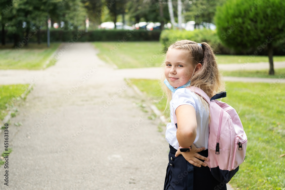 Fototapeta premium blonde curly schoolgirl puts of protective mask in school uniform with pink backpack back to school