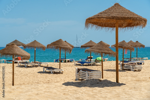 View of the luxury beach on the sea with sun loungers and umbrellas, in the tourist zone of the tropics. In the background is a yacht sailing ship.