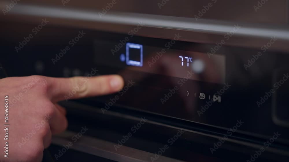 Close-up male hand reducing heat in oven pressing touchscreen button. Unrecognizable Caucasian man adjusting temperature on household appliance indoors Close-up male hand reducing heat in oven pressing touchscreen button. Unrecognizable Caucasian man adjusting temperature on household appliance indoors