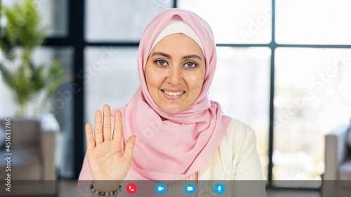 Video meeting with Arabian woman wearing hijab, looking at camera, muslim female employee with covered head takes a part in virtual conference, seminar, waving hand