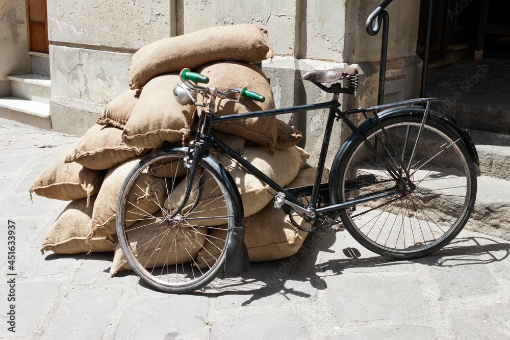 Vintage bicycle leaning against a pile of burlap sacks on the street.