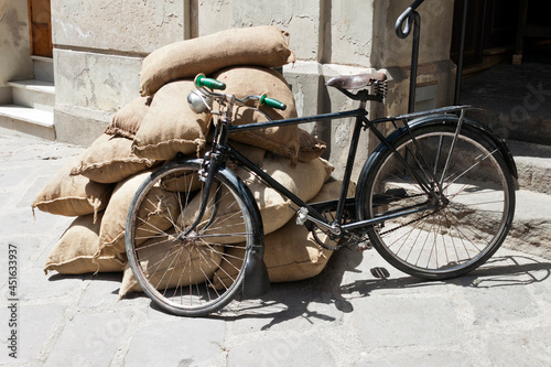 Vintage bicycle leaning against a pile of burlap sacks on the street.