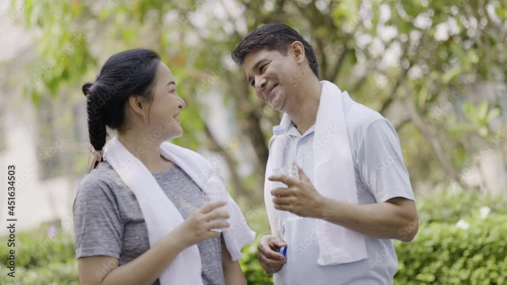 Elderly Asian couple exercising in village garden with happy smiles. Workout makes you healthy. Drink water in plastic bottles are clean from sweat. Weekend activity happy family lifestyle concept. Elderly Asian couple exercising in village garden with happy smiles. Workout makes you healthy. Drink water in plastic bottles are clean from sweat. Weekend activity happy family lifestyle concept.