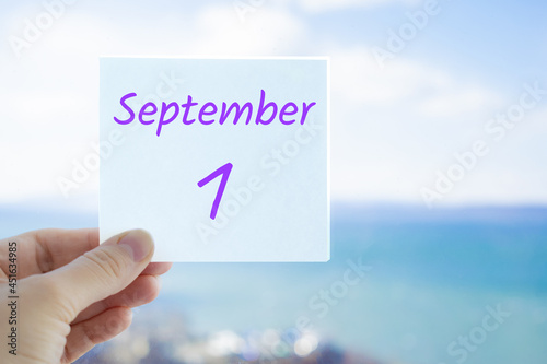 1st September. First day of autumn. Knowledge day. Hand holding sticker with text September 1 on the blurred background of the sea and sky. Copy space for text. Month in calendar concept