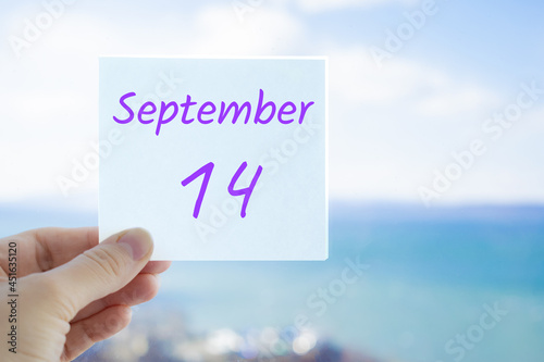14th September. Hand holding sticker with text September 14 on the blurred background of the sea and sky. Copy space for text. Month in calendar concept