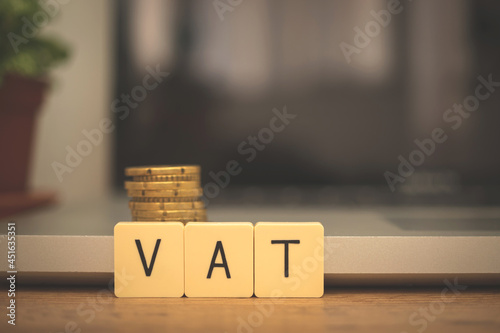 VAT increase concept. Value added tax on wooden block cubes. Business desktop with laptop and coins, management and investment background photo