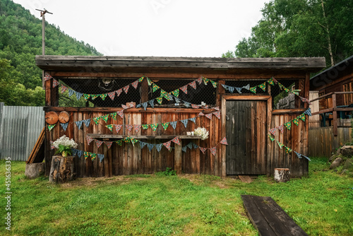 Wooden shed or hut is decorated with colorful triangle flags and bouquet of white gypsophila flowers. Preparing for the celebration of the holiday outdoors in the hot summer photo