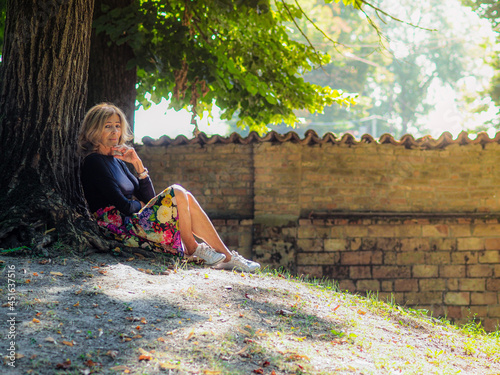 senior blond caucasian woman relaxing on a tree in the park in autumn photo