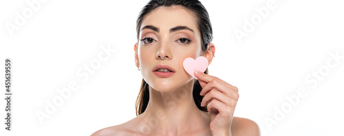 pierced young woman with bare shoulders holding heart-shape sponge isolated on white, banner