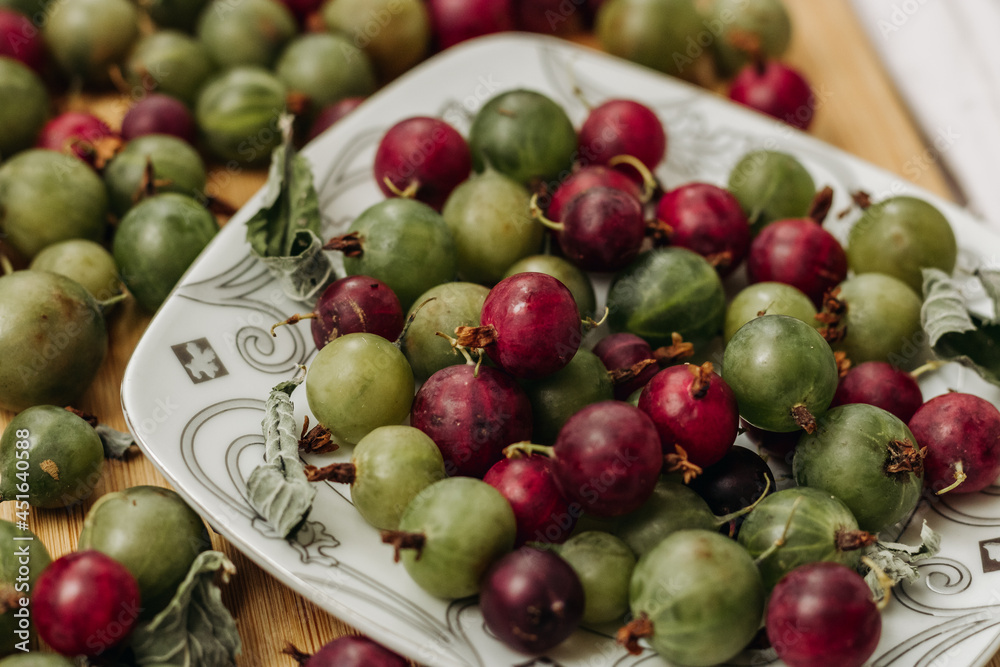 Green and red gooseberries. Gooseberries on a wooden surface and on a white plate. A plate with gooseberries. Dry mint leaf Green and red gooseberries. Gooseberries on a wooden surface and on a white plate. A plate with gooseberries. Dry mint leaf