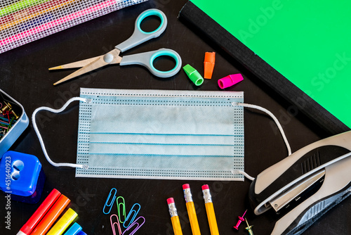 School supplies and face mask on black chalkboard
