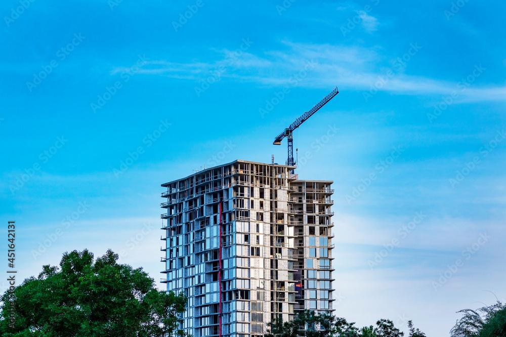 The construction crane and the building against the blue sky. Construction of a high-rise building with a crane. New modern exterior apartment building complex . 