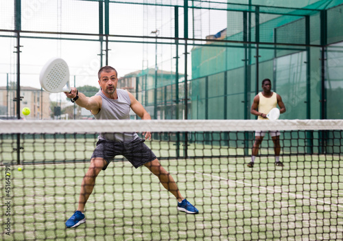 Athletic mens plays padel. View through the tennis net