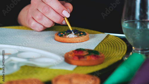 Cookies art decorating: woman painting cookies with brush and food colors on palette