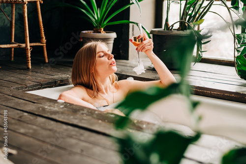 Beautiful young woman drinking champagne and looking to the camera enjoying bubble bath photo