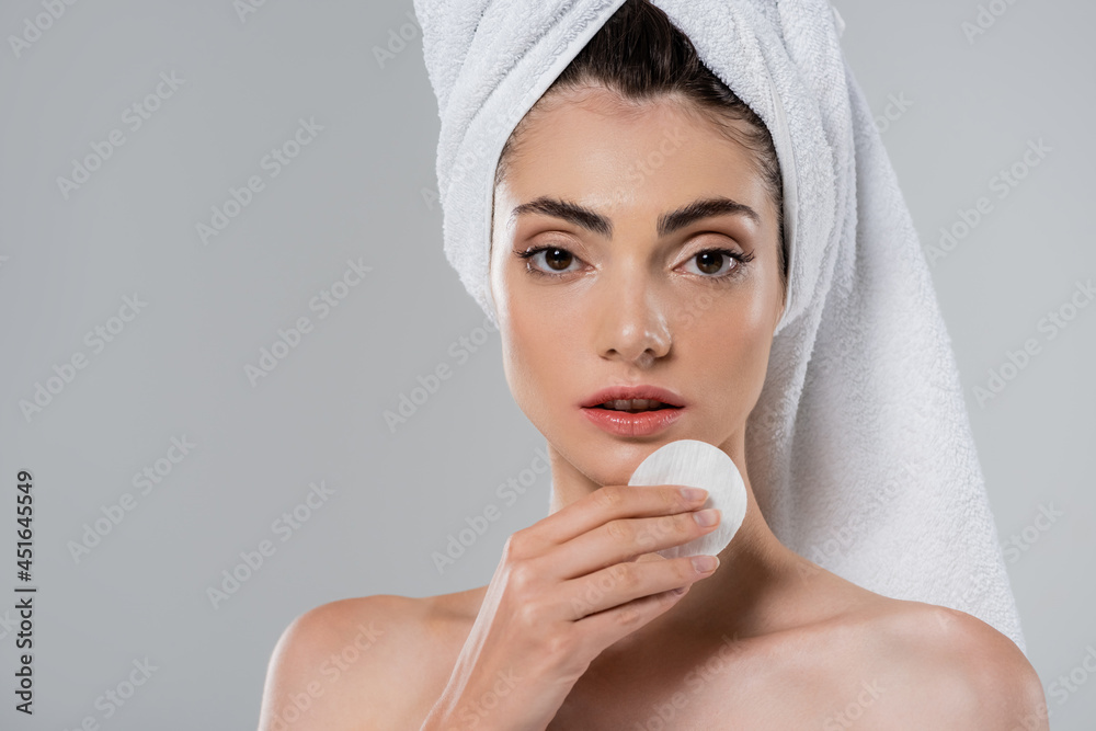 young woman with towel on head removing makeup with cotton pad isolated on grey young woman with towel on head removing makeup with cotton pad isolated on grey