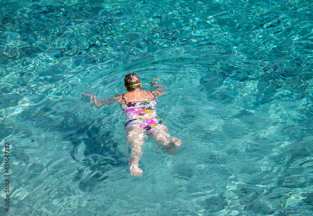 A woman on vacation swimming in the crystal clear turquoise sea.