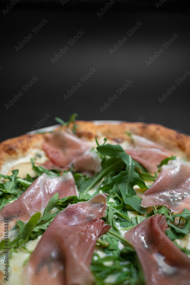 closeup of italian pizza with prosciutto, arugula and cheese on black background closeup of italian pizza with prosciutto, arugula and cheese on black background