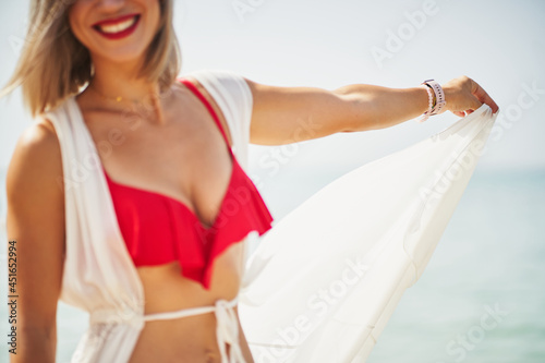 Detail of unrecognizable woman in beach holding her dress and smiling to camera