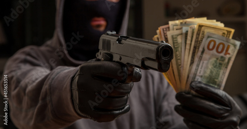 Gloved hand holding a pistol stealing money, closeup view. Armed robbery concept