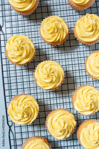 Vanilla cupcakes with yellow frosting on a cooling rack on a blue background