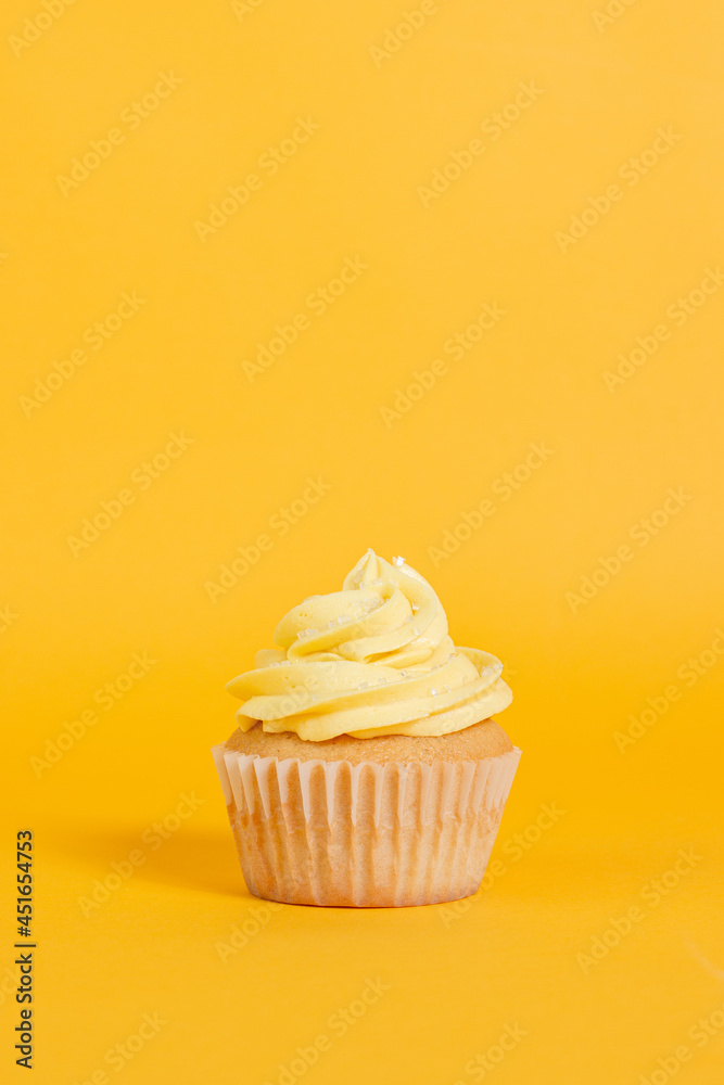 Vanilla cupcake with yellow frosting on a bright yellow background Vanilla cupcake with yellow frosting on a bright yellow background