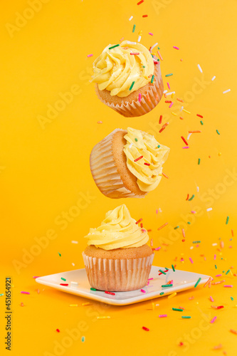 Vanilla cupcakes with yellow frosting and rainbow sprinkles floating on a yellow background