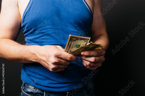a young LGBT student counts the money allocated for her studies. concept: investments and loans. a man in a blue T-shirt holds paper dollars in his hands. unemployment benefits.