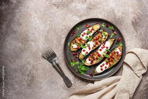 Grilled eggplants with yogurt sauce and pomegranate on a brown grunge background. Top view, flat lay. Middle Eastern and Mediterranean healthy food.