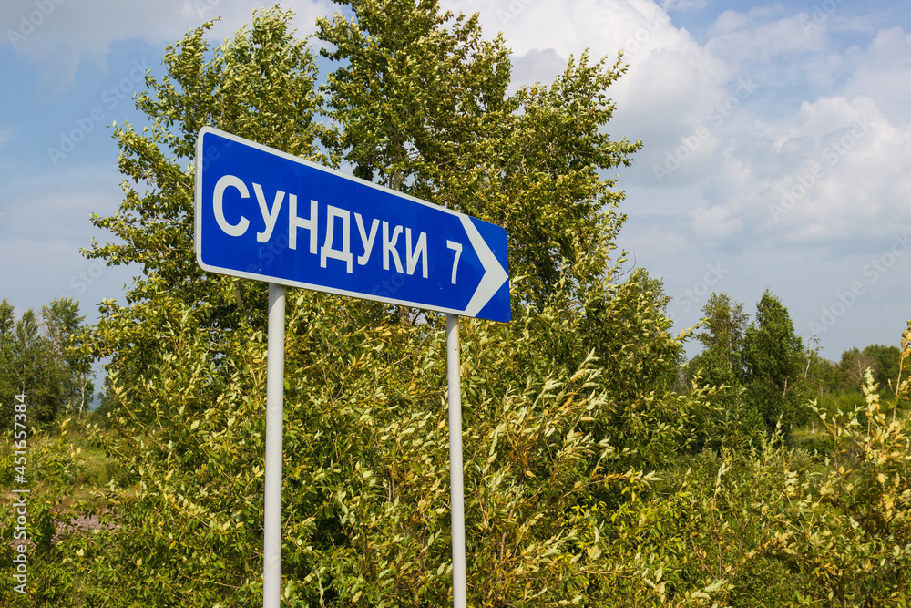 Blue road sign pointing towards Sunduki 7 km. Chests is a mountain range in Khakassia, Russia. The inscription on the plate is translated as 