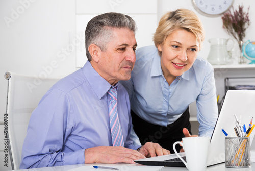 Mature employees looking at interesting news on internet at computer