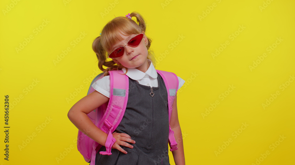 Portrait of beautiful little smiling schoolgirl with backpack wearing sunglasses, charming smile, posing, dancing isolated over yellow studio background wall with copy space. Back to school concept Portrait of beautiful little smiling schoolgirl with backpack wearing sunglasses, charming smile, posing, dancing isolated over yellow studio background wall with copy space. Back to school concept