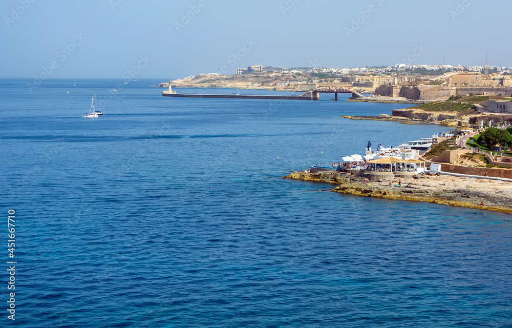 Sliema rocky coastline, Malta, with cafes, bridge and lighthouse.