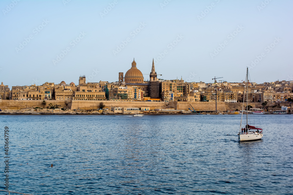 Coastal landscape of Valletta at sunny summer day, with boat in the foreground. Maltese Valletta skyline with church of Our Lady of Mount Carmel and St Paul's Pro-Cathedral.