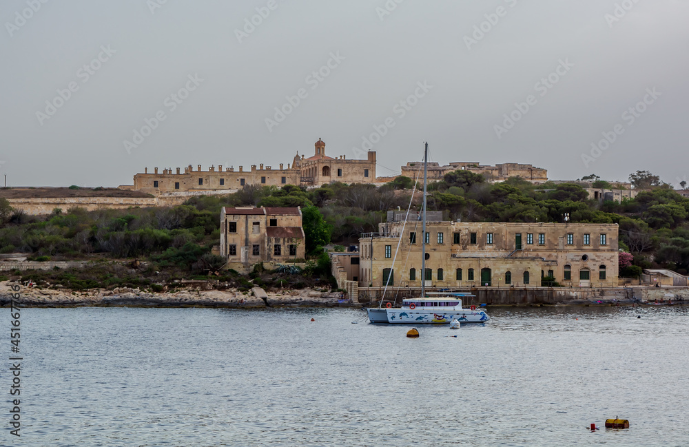 White yacht near old buildings at  Manoel Island in Gzira, Malta, with fort Manoel walls in the background.