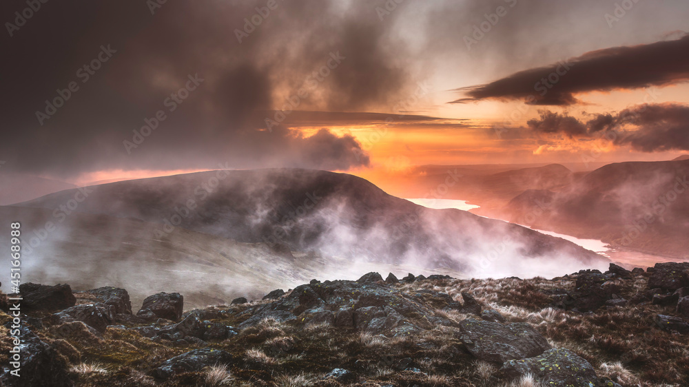 Weather change in Lake District at sunset.Majestic landscape scenery with clouds rolling over the mountain peaks and valley with a lake.View from high up.