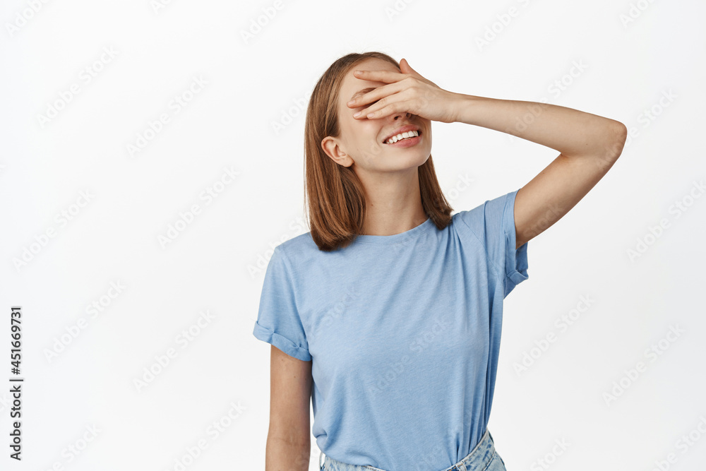 Portrait of beautiful caucasian woman in t-shirt, smiling hopeful, close eyes with hand, waiting for surprise, anticipating gift, standing against white background Portrait of beautiful caucasian woman in t-shirt, smiling hopeful, close eyes with hand, waiting for surprise, anticipating gift, standing against white background