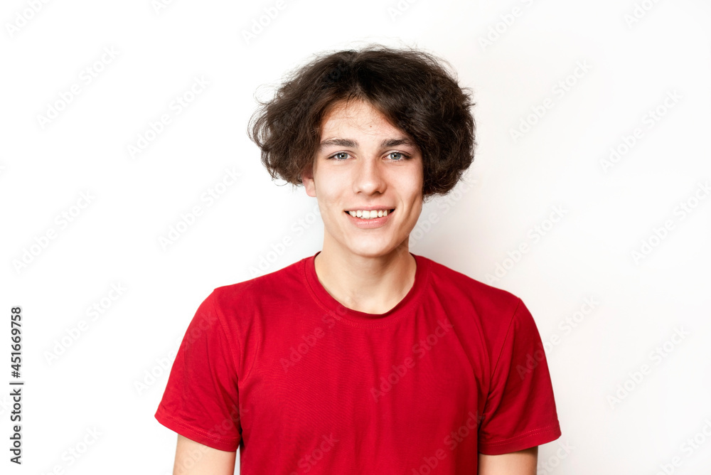 Courageous teenager 16-18 years old with long hair sincerely smiling on a light background. The young man has emotions of happiness and joy on his face, from the joy of entering college Courageous teenager 16-18 years old with long hair sincerely smiling on a light background. The young man has emotions of happiness and joy on his face, from the joy of entering college